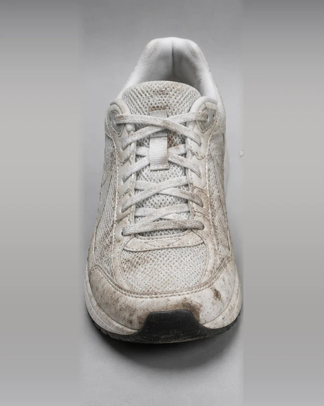 A white trainer before washing, its upper and sole caked in dried mud